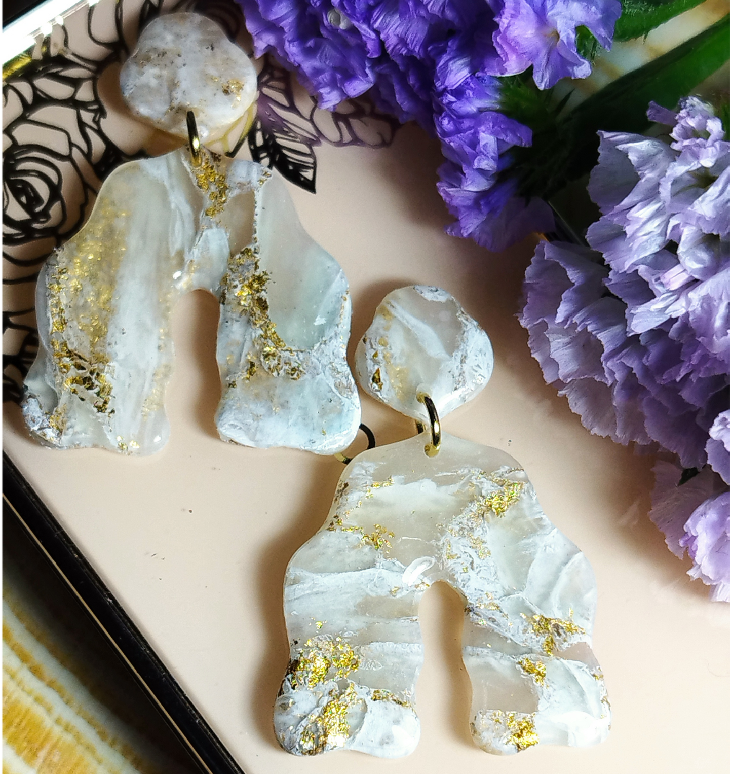 Stella with an Arch Ivory White Quarts Handmade Polymer Clay Earrings. It is a combination of 2 shapes. The first shape is a curvy pentagon attached to a gold jump ring to a curvy arch in ivory white colour with gold sparkles. Stella with an Arch is covered with UV Resin. 