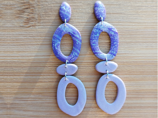 Organic Donut Oval Connected in Royal Purple, Blue Bell and Levander - Purple, Handmade Polymer Clay Earrings. The base of the Earrings is a Donut Oval shape attached to a jump ring to a horizontal abstract oval shape in Levander Purple colour attached to a silver jump ring to a Donut Oval shape hanging from it in Levander Purple colour.