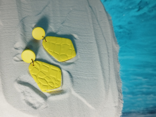 Handmade Polymer Clay Earrings in yellow color. The shape of it is a small yellow circle on the top with a gold jump ring that is attached to a Diamond Trapezoid Shape which has a texture of a snake pattern on it. 